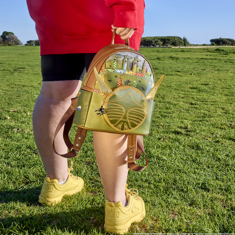 Person wearing a red hoodie and black shorts on a green field, holding the Quidditch mini backpack down by their side by the top handle